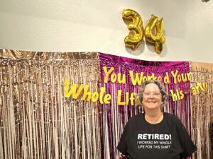 Julie Kane stands smiling in front of a retirement backdrop during her celebration honoring 34 years of service to the Nez Perce Tribe.