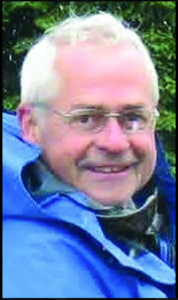 Portrait of Jesse Reece smiling outdoors, wearing glasses and a blue jacket.